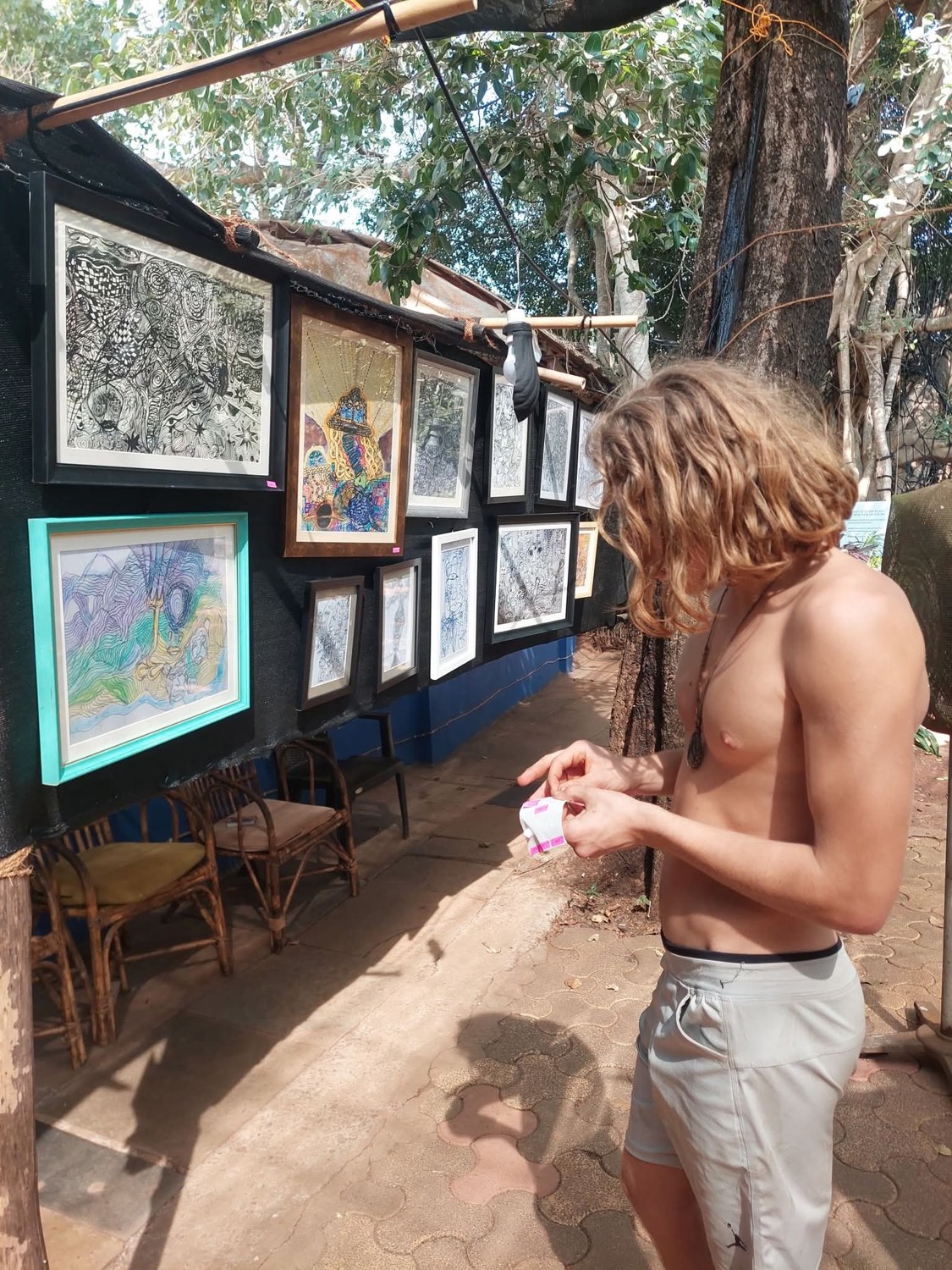 The artist looks closely at his framed drawings hanging on an outdoor display wall.